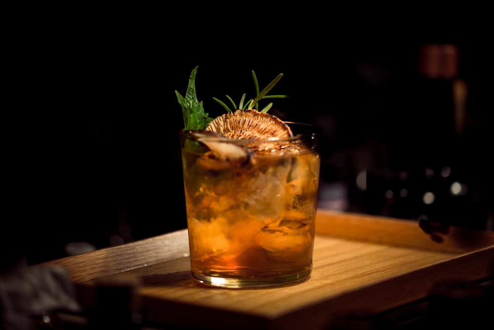 Amber cocktail garnished with herbs on a dark bar